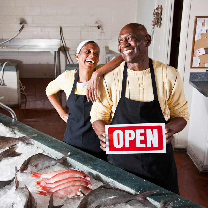 fish market owners holding an "OPEN" sign in their store