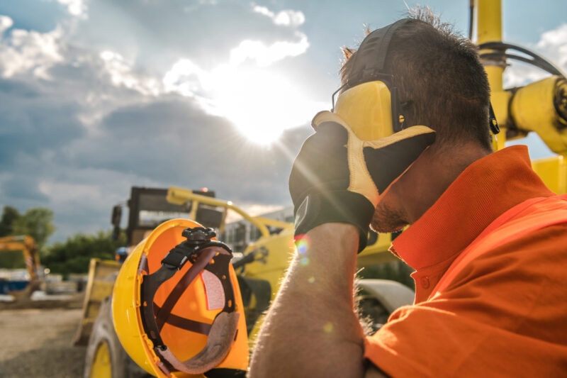 Construction worker wearing hearing protection on a job site with bright sunlight in the background