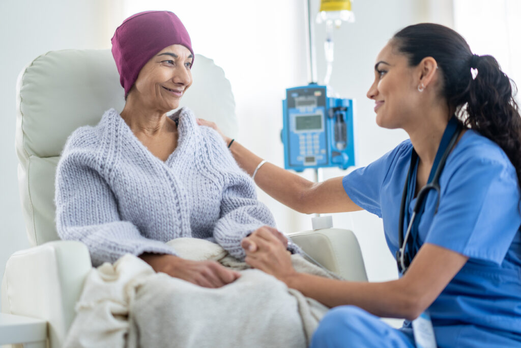 Smiling cancer patient receiving chemotherapy while being comforted by a nurse.