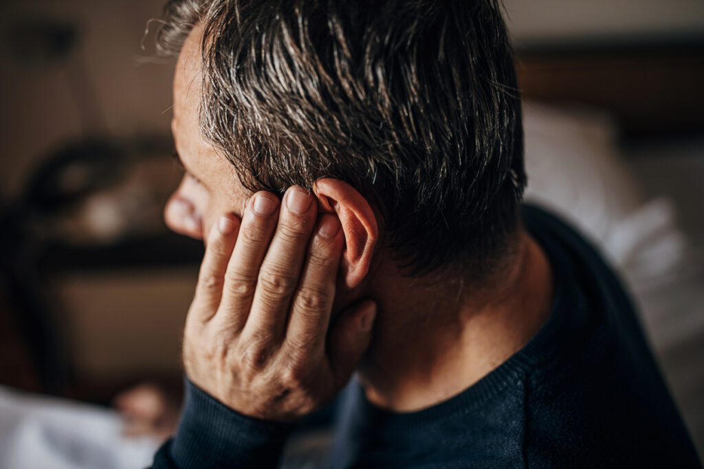 Man holding his ear, indicating hearing concerns related to aging.