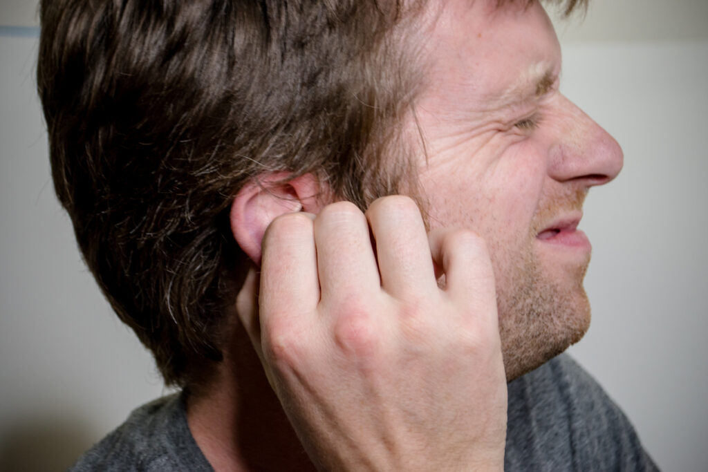 A man grimacing in discomfort while adjusting his hearing aid, indicating frustration or difficulty with its performance.