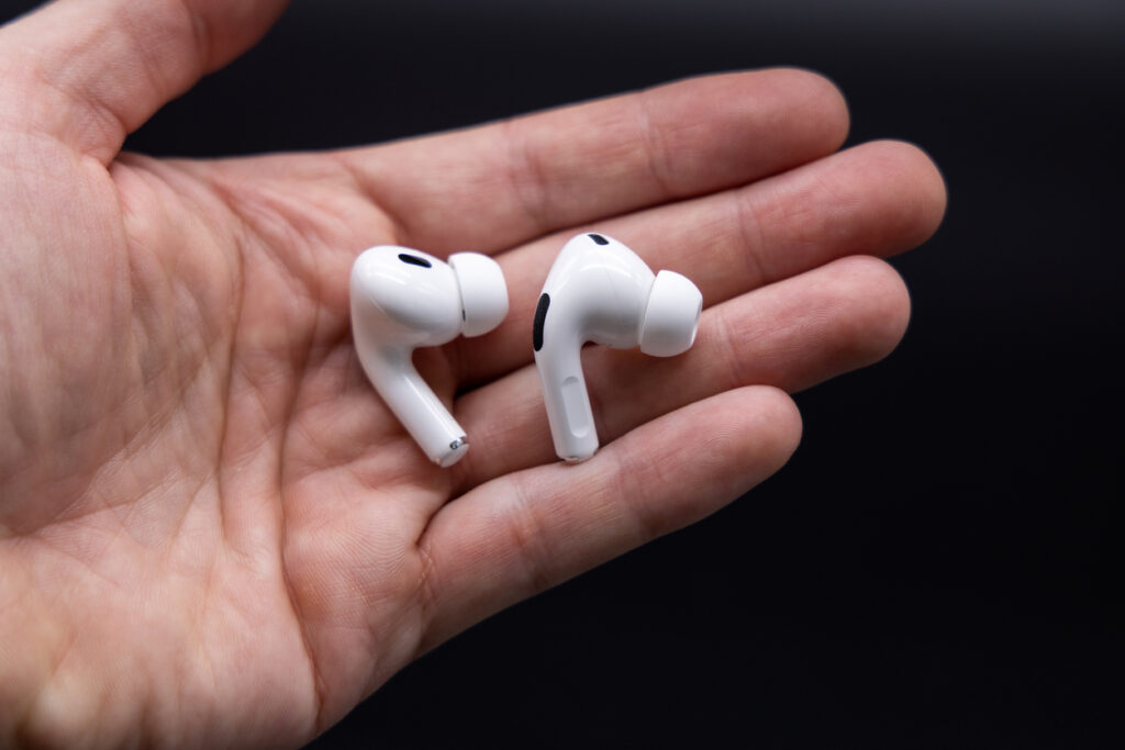 Two white Apple AirPods Pro earbuds held in a hand against a black background.