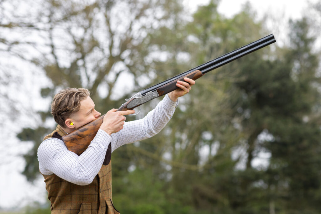 Hunter wearing ear protection while aiming shotgun outdoors