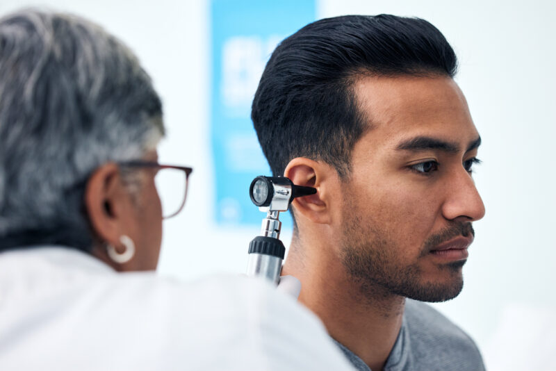 Audiologist examines an adult patient’s ear with an otoscope during a professional ear exam to check for possible earwax blockage.
