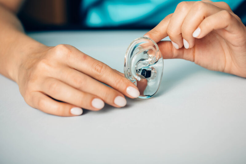Hands holding tiny modern in-canal hearing aid showing 2025 technology advancements