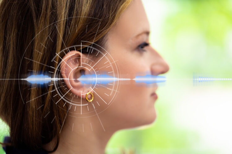 Woman wearing AI-powered hearing aid with digital sound processing visualization and waveform