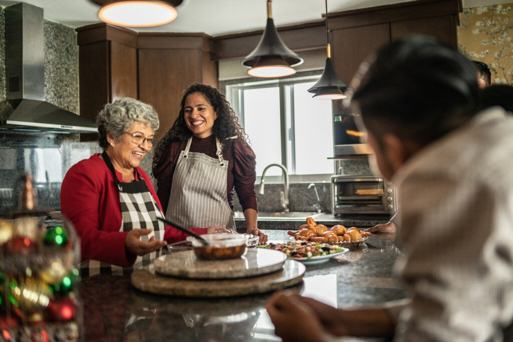 Older woman laughing and cooking with family in a warm kitchen setting