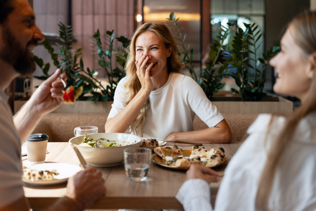 Adults laughing and talking at a restaurant table, illustrating how hearing aid myths can affect social moments at any age.