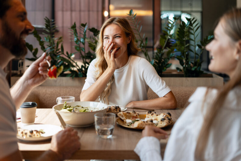 Adults laughing and talking at a restaurant table, illustrating how hearing aid myths can affect social moments at any age.