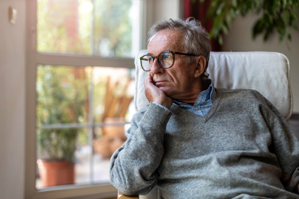 Older man sitting by a window looking tired, illustrating fatigue linked to hearing loss