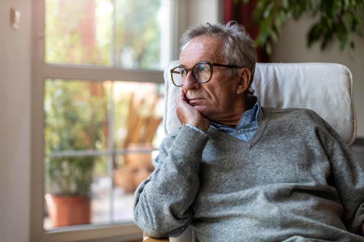 Older man sitting by a window looking tired, illustrating fatigue linked to hearing loss