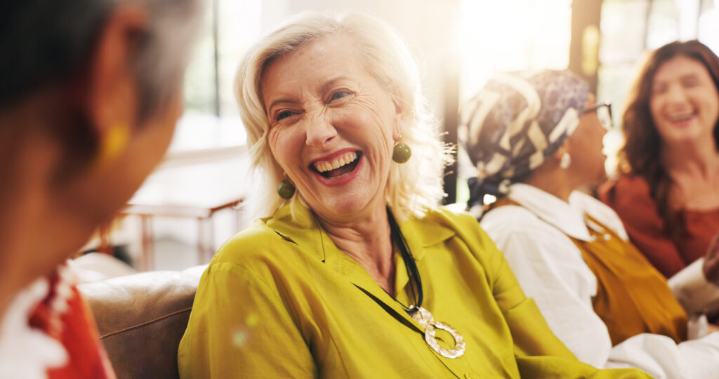 Senior woman laughing and engaging in a lively conversation with friends, showing how clear hearing supports brain health and connection.